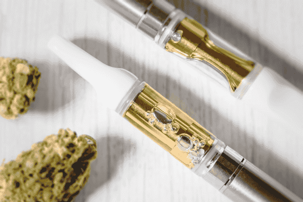Image of cannabis vape cartridges on a wooden surface next to flower nugs.
